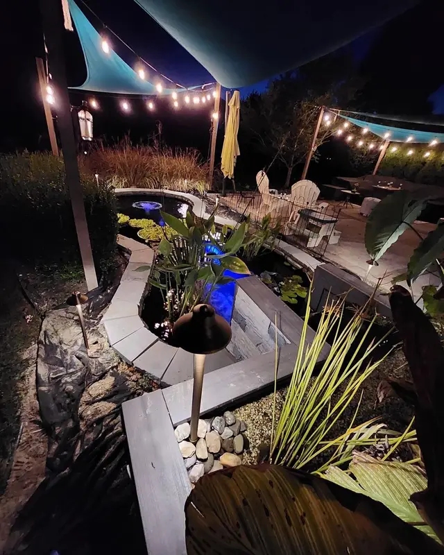 Backyard patio under bistro string lights with lit plantings at night