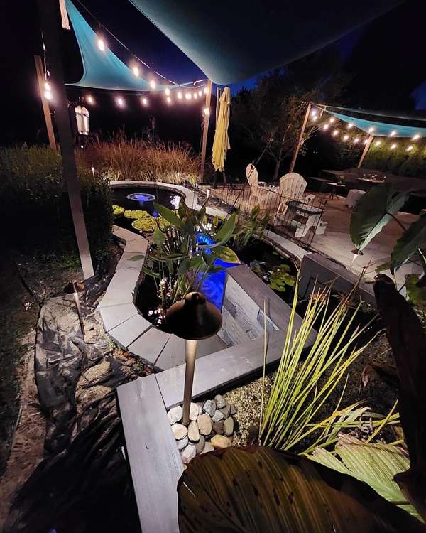 Backyard patio under bistro string lights with lit plantings at night