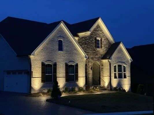 Stone-front two-story home at dusk with warm facade uplighting