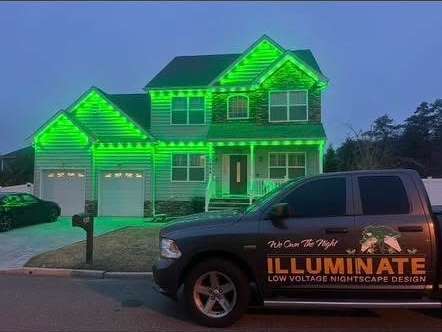 Govee permanent trim lighting in green along the rooflines of a two-story colonial at dusk, with the Illuminate work truck in the driveway