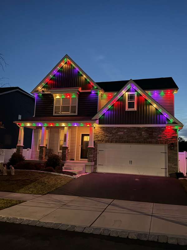 Govee permanent trim lighting in alternating red, green and purple along the gables and porch of a two-story craftsman-style home with a stone front at dusk