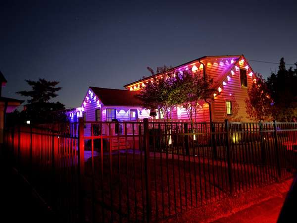 Govee permanent trim lighting in pink, purple and gold on the gables of a home behind a black iron fence at night