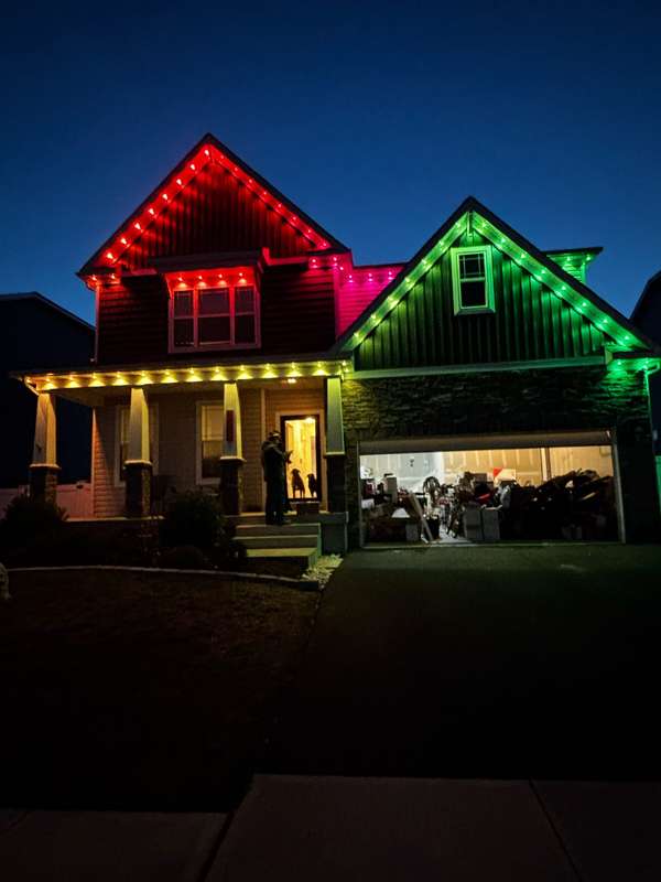 Govee permanent trim lighting in red and green on the twin gables of a craftsman-style home, with gold lights along the porch roof at dusk