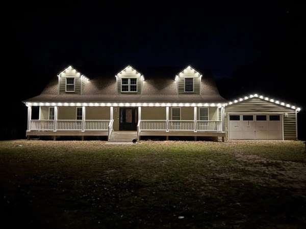 Govee permanent trim lighting in white outlining three roof dormers, the front porch and the garage gable of a farmhouse-style home at night